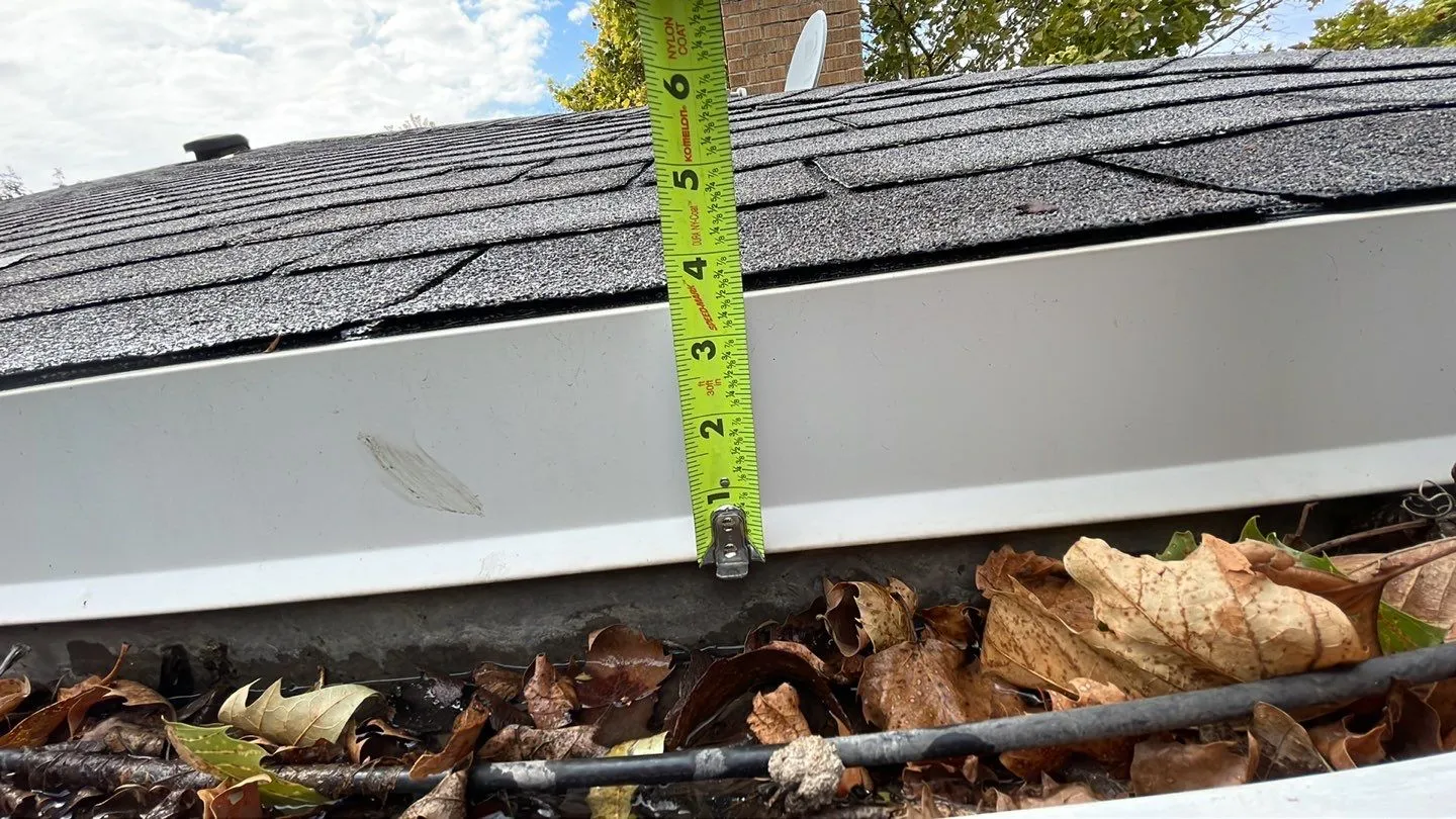 Leaves and debris filling a white gutter beside a shingle roof