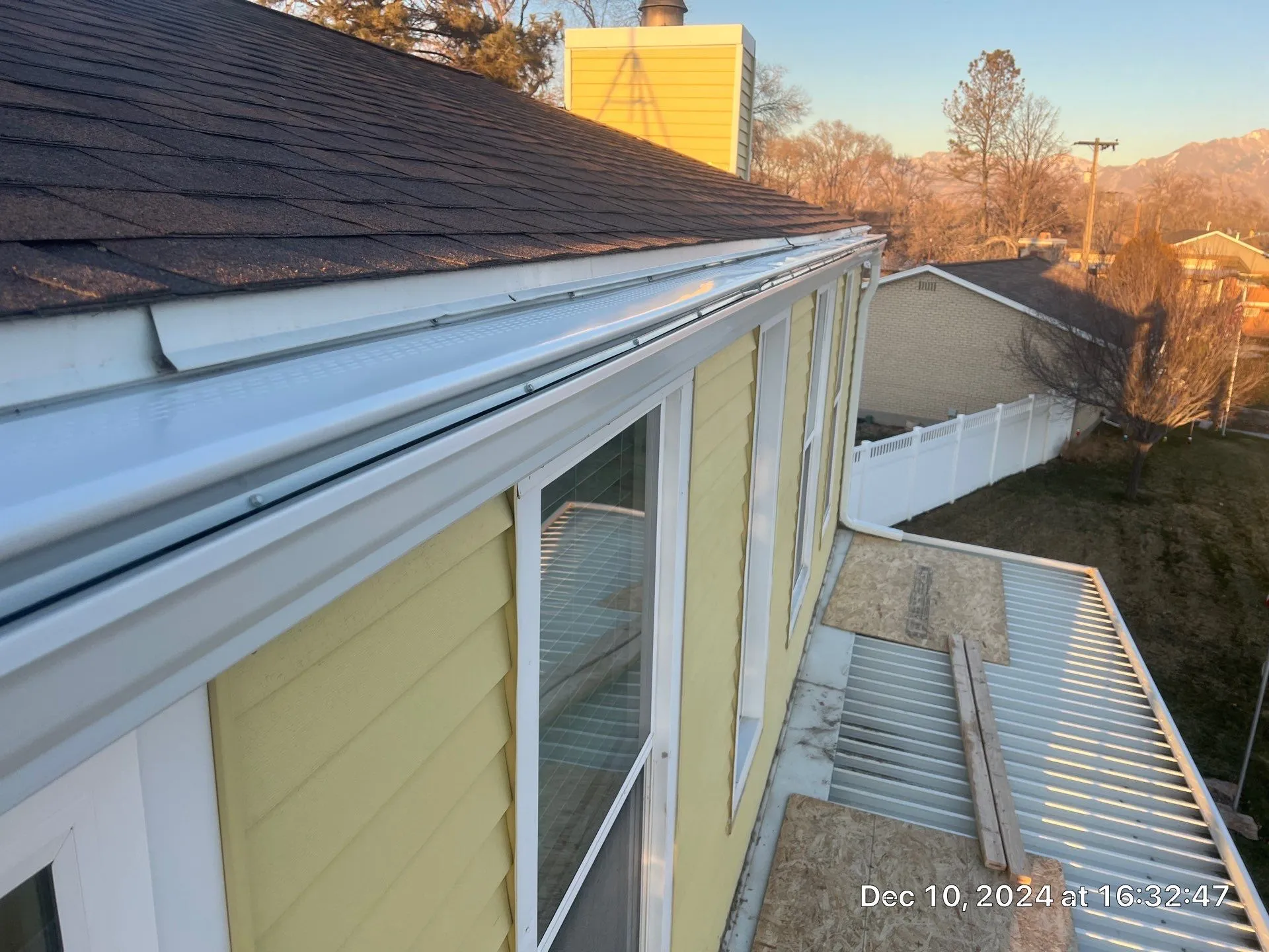Covered white gutter following the edge of a shingle roof